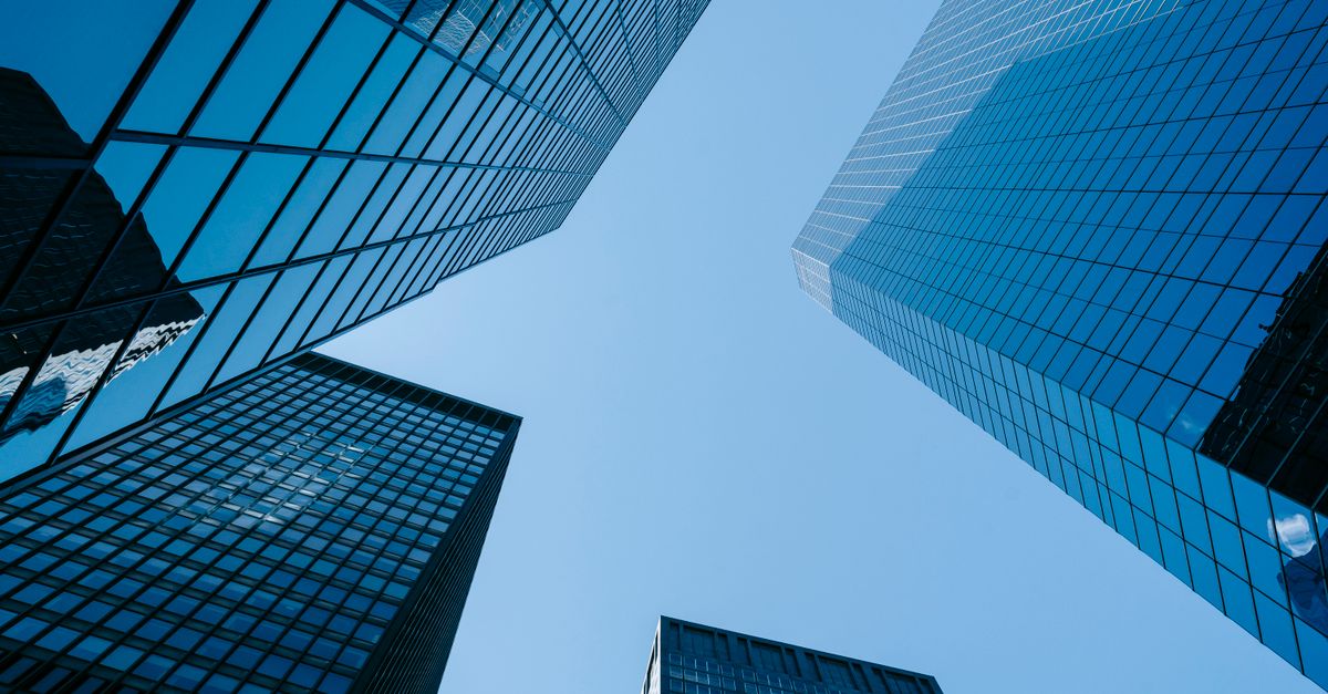 From below of contemporary high rise buildings with glass walls located on street with sunlight in modern district of city